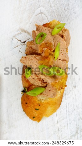 Tapas Bruschetta with Delicious Liver Pate and Crushed Spring Onion on Garlic Bread closeup on White Wooden background. Top View