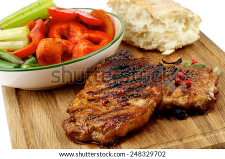 Delicious Roasted Pork Steaks with Vegetable Stocks and Flap of Bread on Wooden Cutting Board isolated on white background. Focus on Steaks