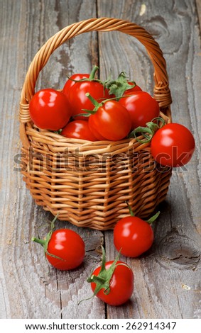 Arrangement of Perfect Ripe Cherry Tomatoes with Stems in Wicker Basket isolated on Rustic Wooden background