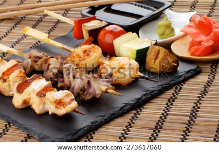 Grilled Salmon, Octopuses, Shrimps and Vegetables on Wooden Stick with Ginger, Soy Sauce and Wasabi closeup on Straw Mat background