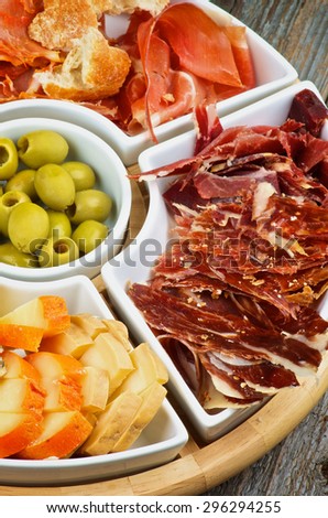 Arrangement of Spanish Snacks with Various Cheeses, Jamon, Cured Ham and Green Olives on Serving Plate closeup on Wooden background