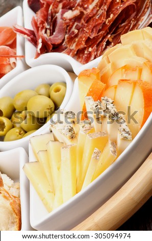 Serving Plate with Delicious Spanish Cheeses, Cured Ham, Green Olives and Bread closeup. Focus on Foreground
