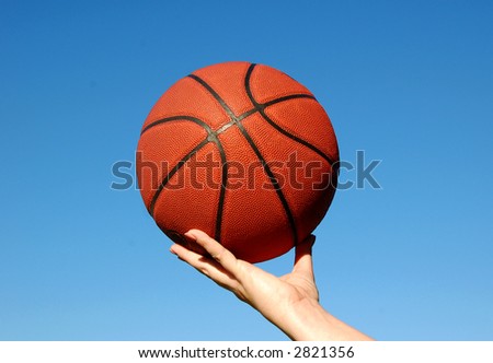 basketball being held in hand against a brilliant blue sky