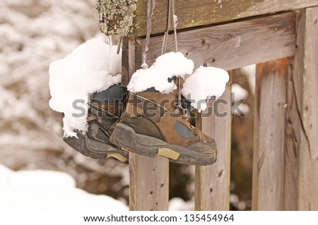 a pair of snow-covered hiking boots hanging on a wooden fence