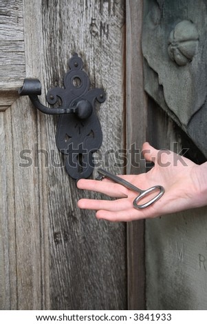 Old solid castle door of solid oak and hand holding the huge key.