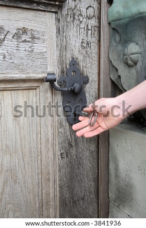 Unlocking heavy castle door of solid oak with a huge key.