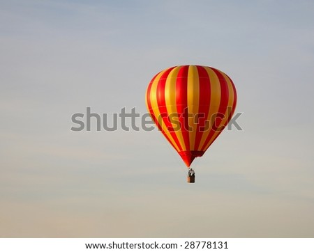 Red and yellow striped hot air balloon on a blue sky with purple clouds.