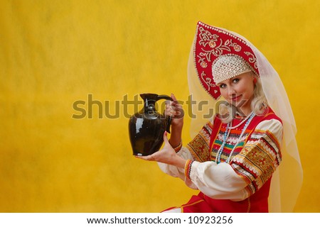 Russian woman in a folk russian dress holds a jug on yellow background