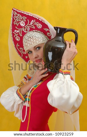 Close-up. Woman in a folk russian dress holds a jug on yellow background