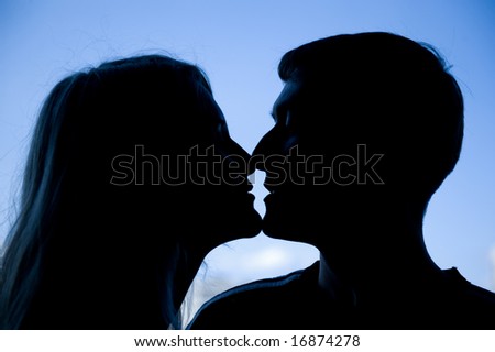 Silhouette of a young couple kissing on blue sky