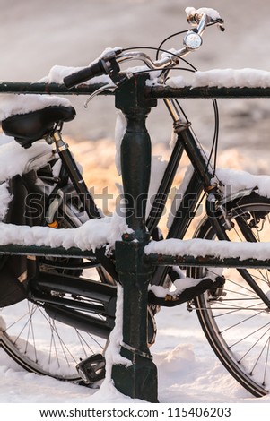 Black lady bicycle covered with snow on a canal bridge in Amsterdam