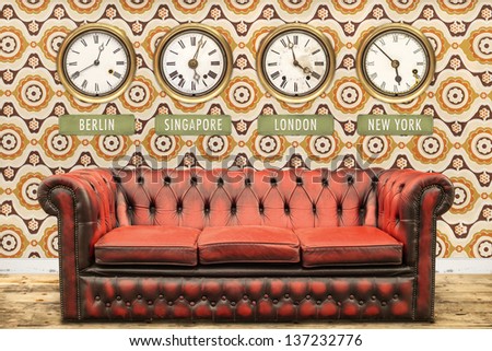 Retro chesterfield sofa with world time clocks on a wall with vintage wallpaper
