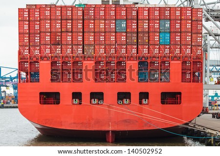 Back of a red container ship filled with red containers in a harbor
