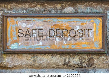 Weathered copper bank placard with the text safe deposit on an ancient brick wall