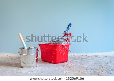 Light blue painted wall with painting tools in front on a concrete floor