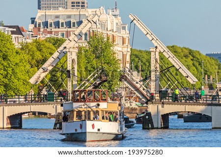 AMSTERDAM, THE NETHERLANDS - MAY 16, 2014: A vintage cruise boat passes the famous Amsterdam Skinny Bridge crossing the Amstel river