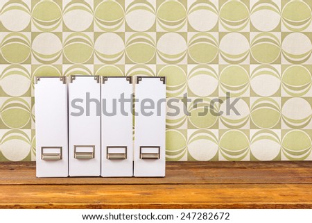 Four white magazine files on a wooden shelf in front of retro green wallpaper