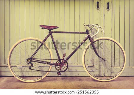 Retro styled image of a rusted racing bicycle parked in an old factory with wooden doors