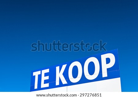 Large real estate sign with the Dutch text \'for sale\' in front of a clear blue sky