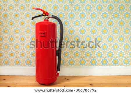 Fire extinguisher on an old wooden floor in front of retro flower wallpaper