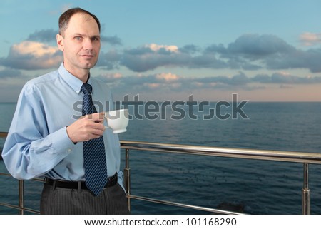 Businessman drinking coffee on a balcony against a sea