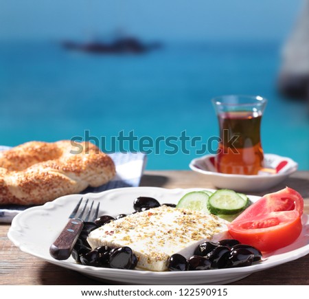 Breakfast with feta cheese, olives, simit, vegetables and tea against Mediterranean sea