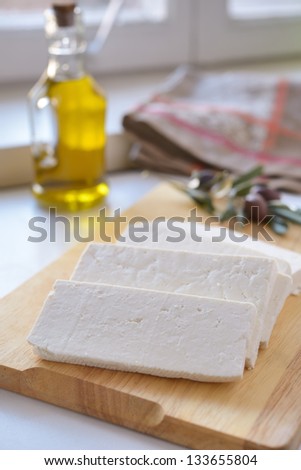 Feta cheese on a cutting board against olives and olive oil