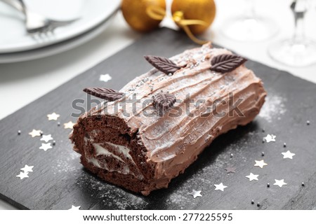 Yule log cake decorated with chocolate leaves on a Christmas table