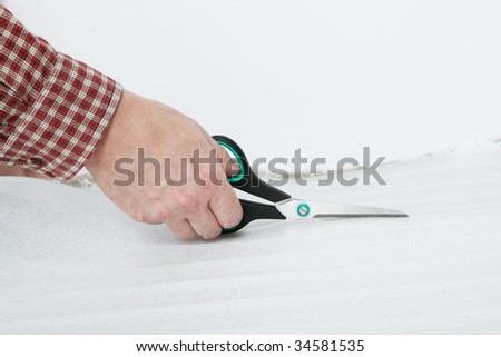 Man\'s hand with scissors cutting the underlay for the laminate flooring installation