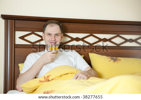 Adult man drinking orange juice in the bed