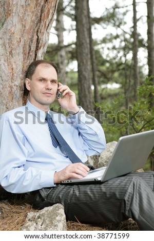 Businessman with laptop and mobile phone in the forest