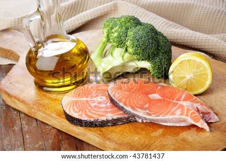 Raw salmon steaks, broccoli, lemon, and olive oil on a wooden cutting board