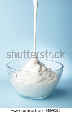Sour cream pouring in a glass bowl against blue