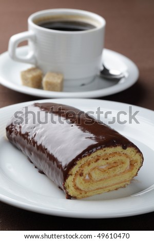 Swiss roll with cream filling and chocolate topping against a cup of black coffee