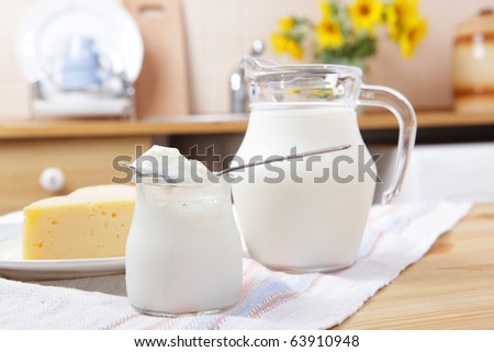 Yogurt, yellow cheese, and the jug of milk on a kitchen table