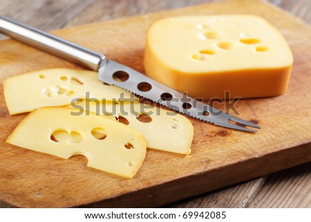 Sliced cheese and cheese knife on the wooden cutting board