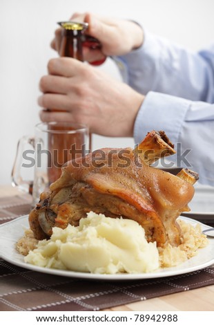 Man eating eisbein with braised cabbage, mashed potato, and beer