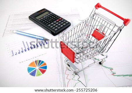 Shopping basket toy on business documents background. E-commerce concept.