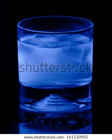 glass of iced tonic water glows blue under ultraviolet black light