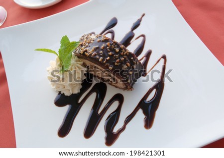 oblique view of chocolate ice cream roll with nuts and chocolate sauce , garnished with whipped cream and mint sprig