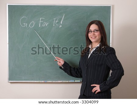 female teacher with glasses, long brown hair, smiling, points to inspirational message, \