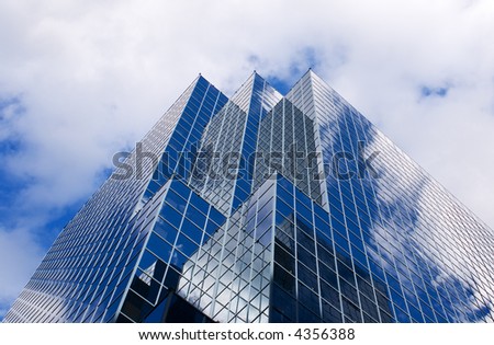 Glass skyscraper against cloudy blue sky; strongly reflective windows; angular view from base