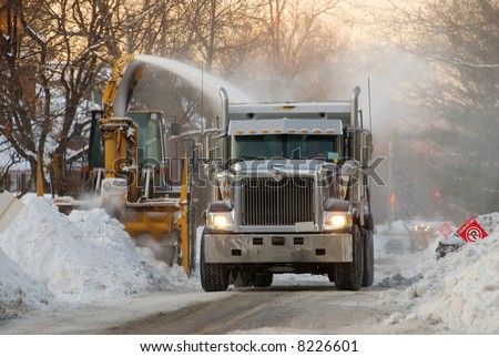 Municipal snow removal crew at work; snow thrower and dump truck on street of snow