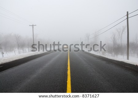 Approaching headlights in heavy fog on road in winter; wide angle view