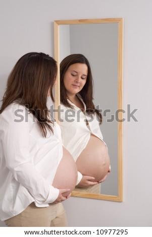 pregnant young woman examines her belly in the mirror