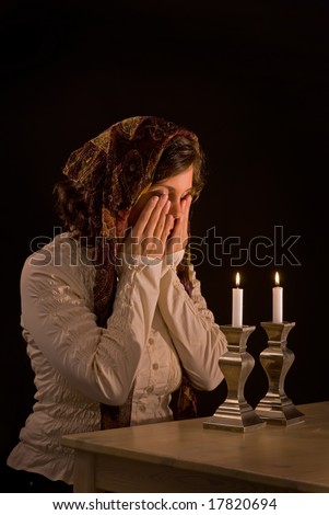Jewish woman says blessing upon lighting candles, covering eyes in traditional manner. unsharpened