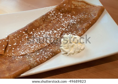 A folded crepe with powdered sugar and a dollop of whipped cream on a rectangular white plate