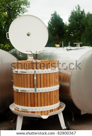 Wooden grape press for making wine, beside steel storage tanks