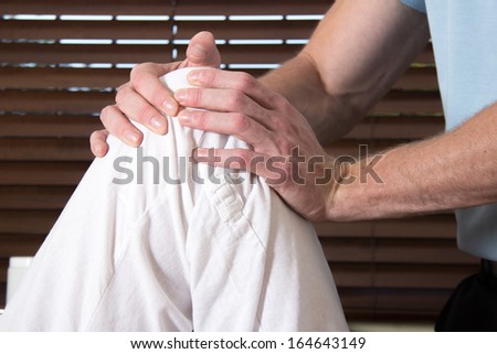 Chiropractor treating knee of female patient with his hands