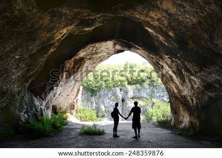 Man and woman holding each other\'s hands in front of the cave entrance